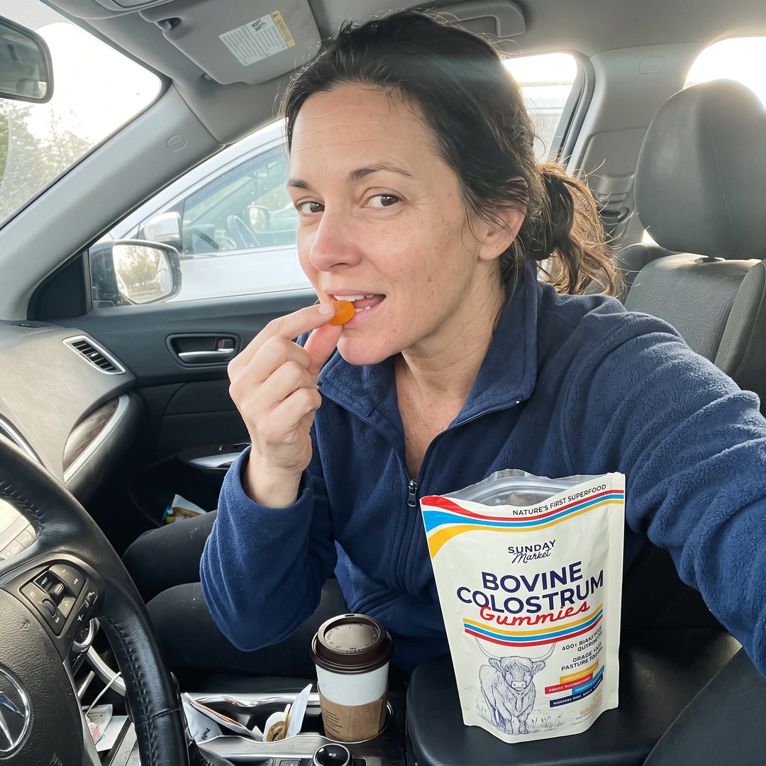 Woman taking a Sunday Market colostrum gummy in her car with the bag on the console